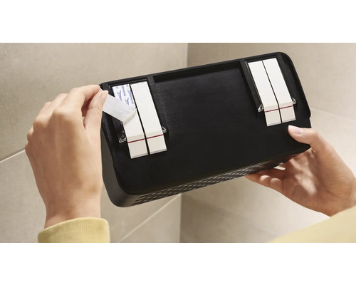 Osoba připevňuje černou nástěnnou polici lepicími proužky na stěnu