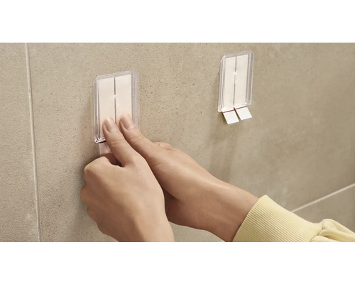 Osoba připevňuje lepicí háček na zeď