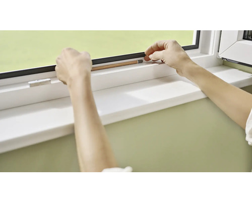 Osoba měří okno tužkou.