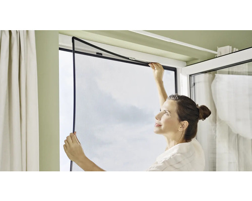 Žena instaluje do okna síť proti hmyzu