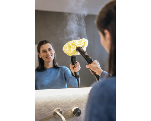 Žena používá parní čistič se žlutým látkovým nástavcem na zrcadlo v koupelně