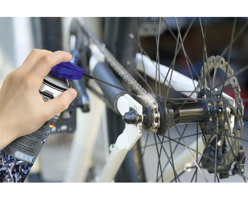 Osoba maže řetěz kola sprejem na řetězy.