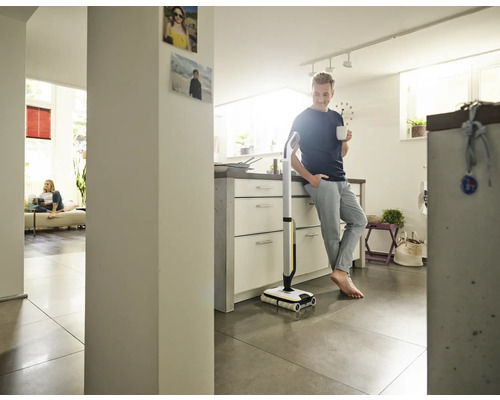 Muž se opírá o kuchyňskou linku s šálkem v ruce vedle elektrického mopu.