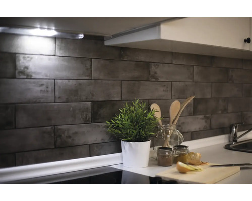 Kuchyňská scéna s obkladem stěn se vzhledem kamene, rostlinou a kuchyňským náčiním na pracovní desce.