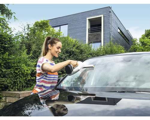Žena čistí čelní sklo automobilu pomocí okenního vysavače.