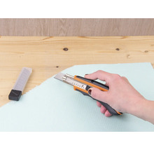 Ruka řeže izolační desku řezačkou.