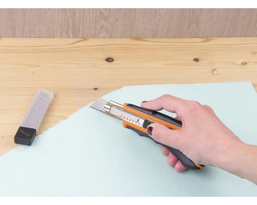 Ruka řeže izolační desku řezačkou.