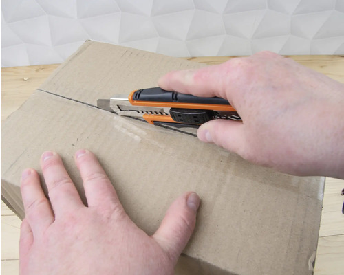 Osoba otevírá kartonovou krabici pomocí odlamovacího nože.