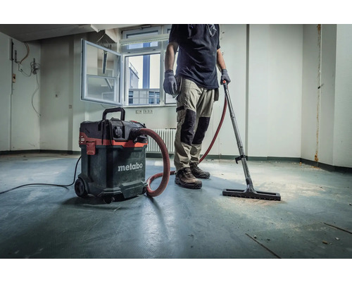 Řemeslník s průmyslovým vysavačem Metabo k čištění místnosti.