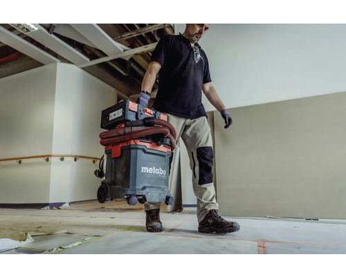 Řemeslník nese průmyslový vysavač Metabo s příslušenstvím místností.
