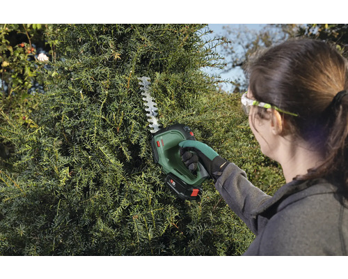 Žena stříhá živý plot pomocí akumulátorových nůžek na živý plot