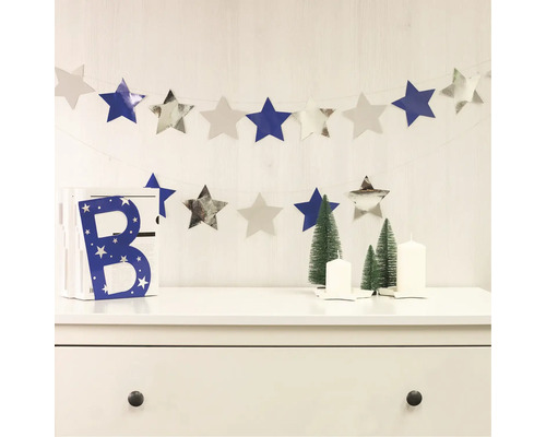 Dekorativní scéna s hvězdnou girlandou, ozdobným písmenem, vánočními stromky a svíčkami na komodě