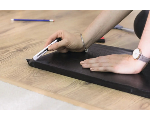 Řezání soklové lišty ořezávačem na dřevěné podlaze.