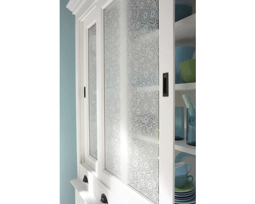 Detail bílé kuchyňské skříňky se skleněnými dvířky s květinovým vzorem.