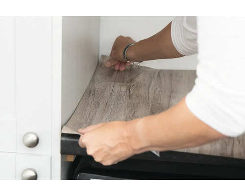 Osoba aplikuje nábytkovou fólii s dřevěným vzhledem v kuchyni.