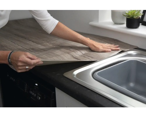 Žena nanáší dekorativní fólii s dřevěným vzhledem na kuchyňskou pracovní desku