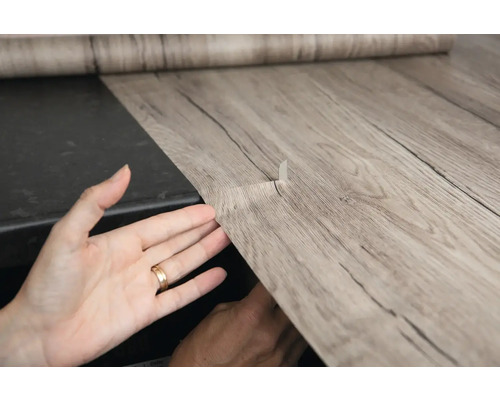 Samolepicí fólie s dřevěným vzhledem se aplikuje na povrch.