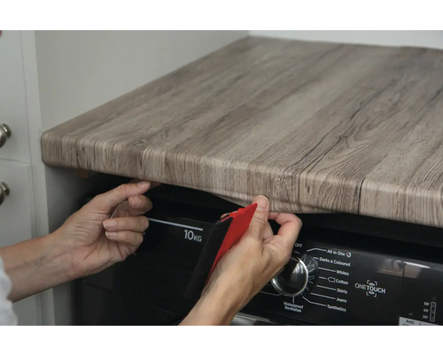 Osoba nanáší samolepicí fólii s dřevěným vzhledem na pracovní desku