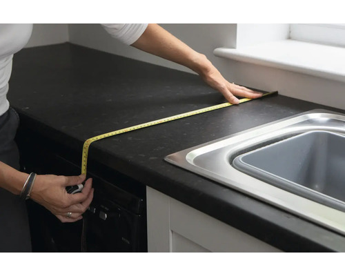 Osoba měří kuchyňskou linku svinovacím metrem.