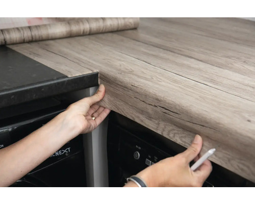 Kuchyňská scéna s osobou, která aplikuje samolepicí fólii na kuchyňskou linku.