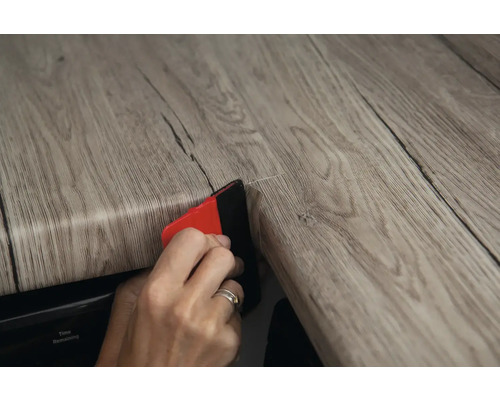 Osoba nanáší dekorativní fólii na povrch pomocí stěrky