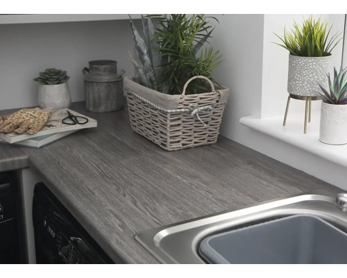Pracovní deska s dřevěnou strukturou, umyvadlo a dekorativní prvky jako rostliny a košíky.