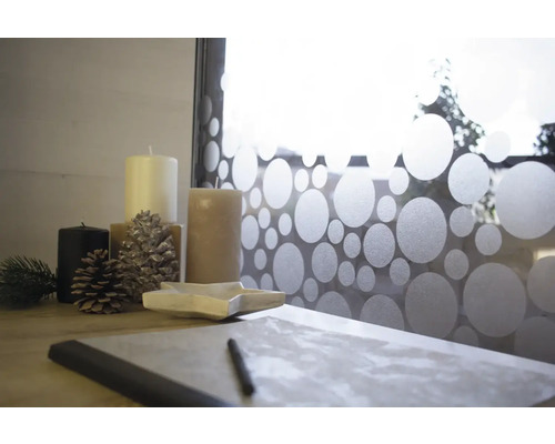 Dekorativní uspořádání se svíčkami, šiškami, miskou ve tvaru hvězdy a zápisníkem na stole před oknem s fólií se vzorem teček.