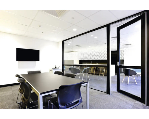 Světlá konferenční místnost se skleněnou přepážkou, stolem, židlemi a obrazovkou.