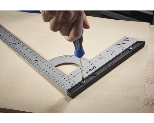 Logo Wolfcraft. Osoba připevňuje multifunkční úhelník k dřevěné desce pomocí šroubováku.