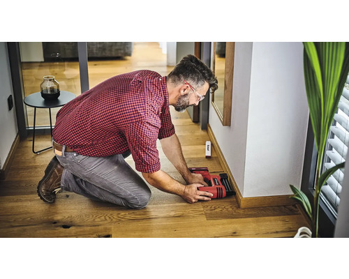 Muž připevňuje soklové lišty ke zdi pomocí elektrické sponkovačky