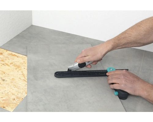 Osoba řeže dlaždice řezačkou dlaždic a řezacím nožem