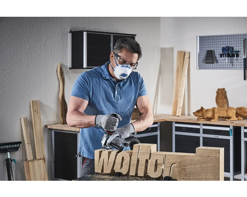 Muž pracuje s dřevoobráběcí frézou na kusu dřeva s nápisem Wolfer, přičemž má na sobě ochrannou masku a ochranné brýle v dílně.