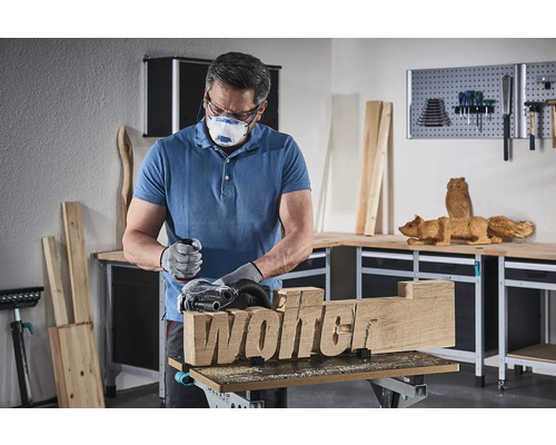 Muž brousí kus dřeva s nápisem Wolter pomocí brusky.