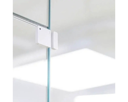 Bílý okenní nebo dveřní kontaktní senzor připevněný ke skleněné desce