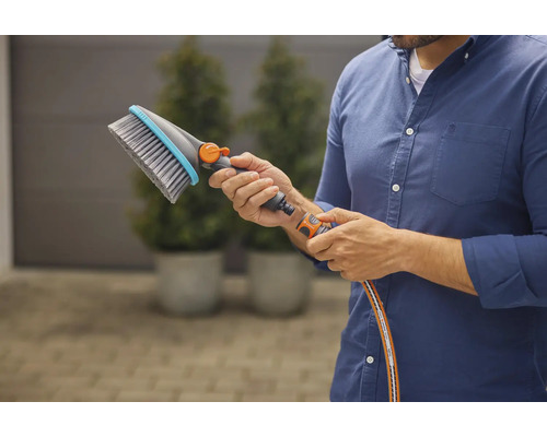 Osoba drží v ruce mycí kartáč s přípojkou na vodu.