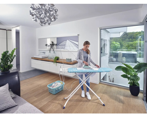 Žena žehlí prádlo na žehlicím prkně ve světlé místnosti.