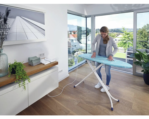 Žena žehlí prádlo na žehlicím prkně ve světlé místnosti.