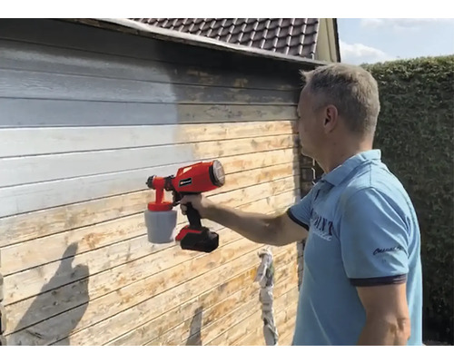 Muž natírá dřevěnou stěnu barvou pomocí stříkacího systému