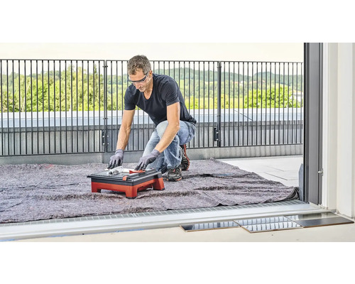 Muž řeže dlaždice řezačkou dlaždic na balkóně.