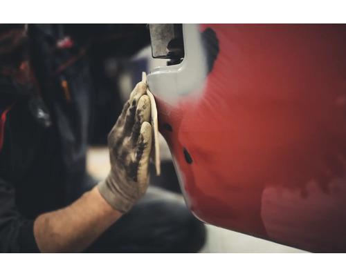 Osoba brousí červené vozidlo smirkovým papírem.