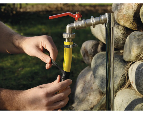 Osoba opravuje zahradní hadici izolační páskou na vodovodním kohoutku.