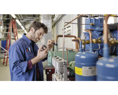 Muž v pracovním oděvu kontroluje chladicí jednotku v technické místnosti.