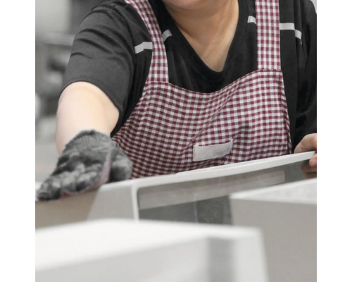 Osoba v zástěře a rukavicích kontroluje keramický výrobek.