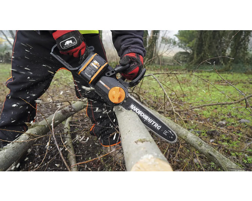 Osoba řeže větev akumulátorovou řetězovou pilou Worx Nitro.