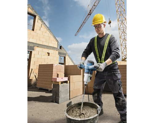 Stavební dělník míchá maltu s elektrickým míchadlem na staveništi.