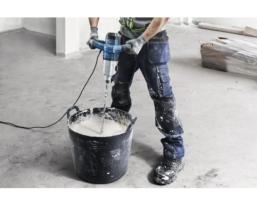 Řemeslník míchá maltu elektrickým míchadlem ve vědru.