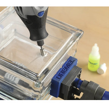 Logo společnosti Dremel. Skleněná dlaždice je vrtána multifunkčním nástrojem Dremel a je upevněna šroubovou svorkou.