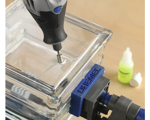 Logo společnosti Dremel. Skleněná dlaždice je vrtána multifunkčním nástrojem Dremel a je upevněna šroubovou svorkou.