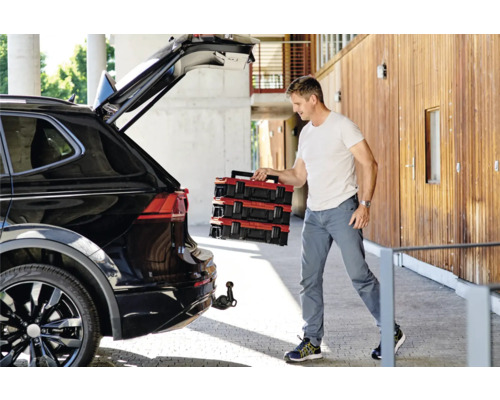 Muž vykládá červené kufříky s nářadím z černého auta