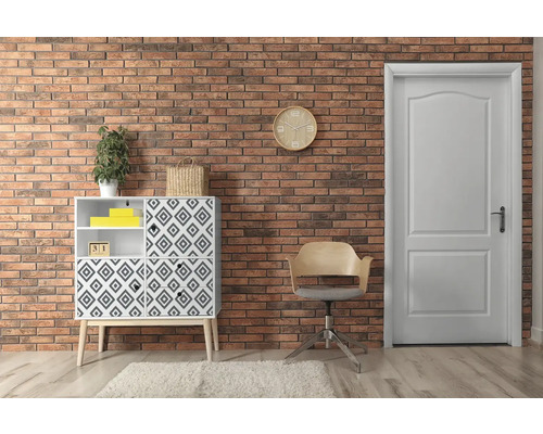 Obývací pokoj s komodou, židlí a dveřmi před cihlovou zdí.